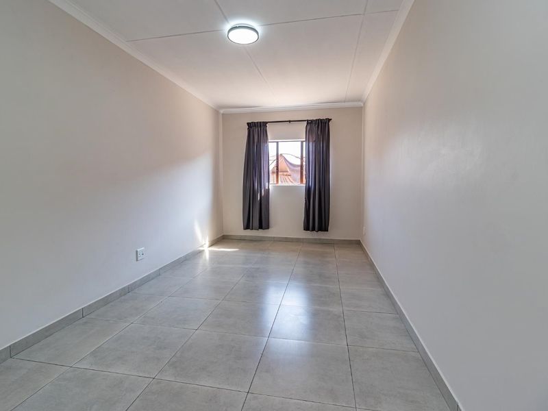 A clean, empty bedroom featuring neutral tiled flooring, smooth walls, and a single window, providing a versatile space ready for personalization.