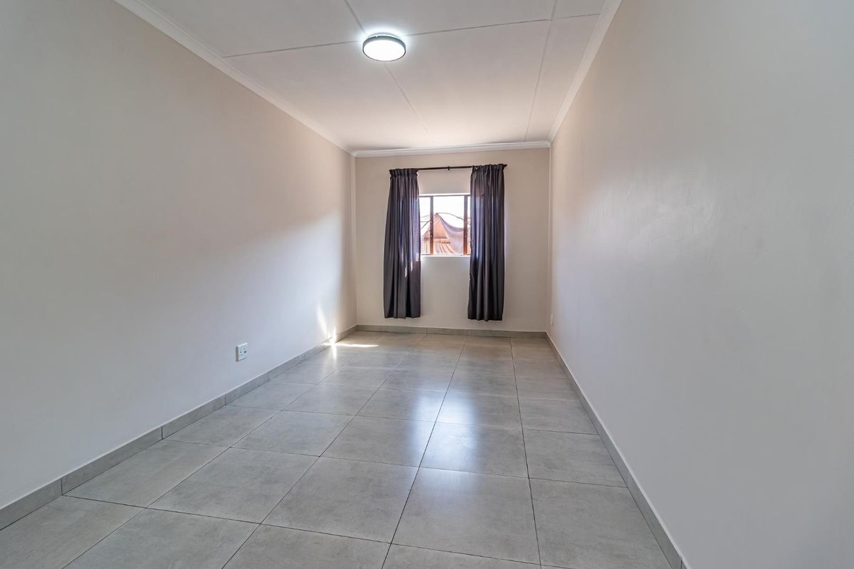 A clean, empty bedroom featuring neutral tiled flooring, smooth walls, and a single window, providing a versatile space ready for personalization.