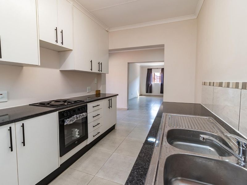 A clean, modern kitchen featuring white cabinetry, dark granite countertops, a built-in oven, and a double stainless steel sink with tiled flooring.