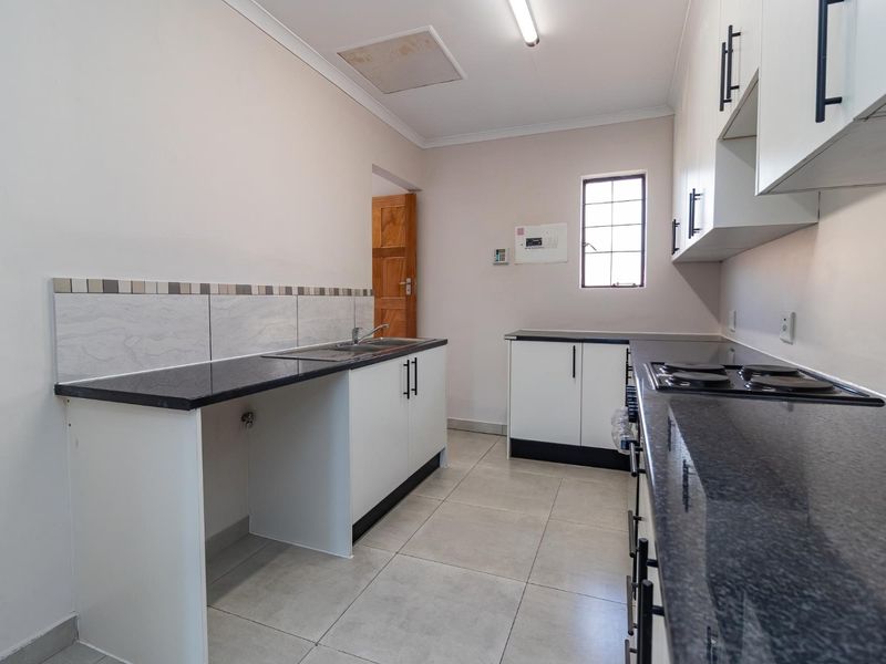 A clean, functional kitchen featuring granite countertops, white cabinetry, an electric hob, and tiled flooring, offering a bright and practical workspace.