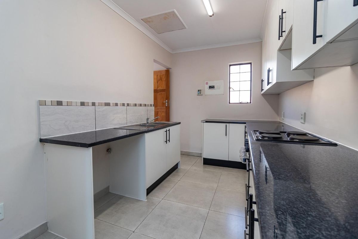A clean, functional kitchen featuring granite countertops, white cabinetry, an electric hob, and tiled flooring, offering a bright and practical workspace.