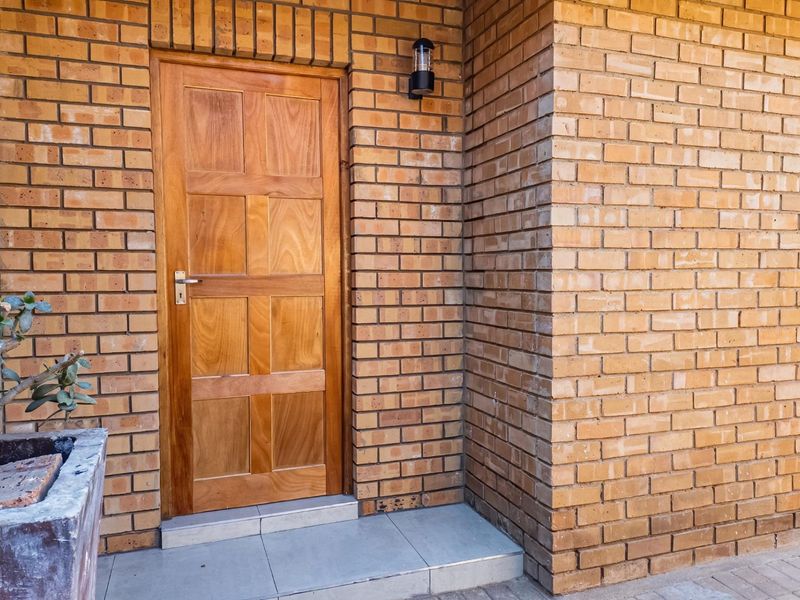 A well-maintained townhouse entrance featuring a classic wooden panel door set within a face brick facade and a modern exterior wall light.
