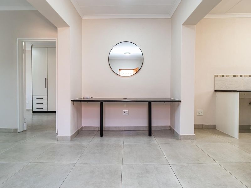 Open plan living area featuring neutral tiled flooring, a built-in desk workspace, and access to adjacent rooms with built-in storage.