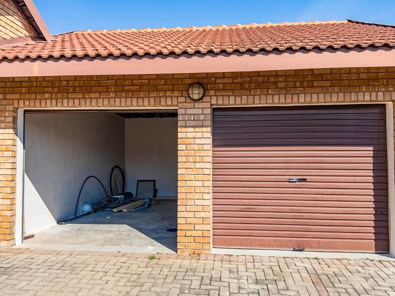 A double garage featuring a brick facade, tiled roof, one enclosed roller shutter door, and one open bay with concrete flooring.
