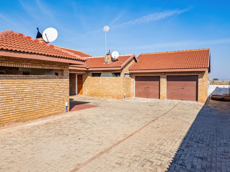 Front exterior view of a townhouse featuring a double garage, brick facade, and a spacious paved driveway under a clear blue sky.