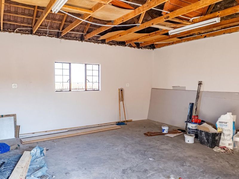 An unfinished garage space featuring exposed timber roof trusses, concrete flooring, and a steel-framed window, currently undergoing renovation.