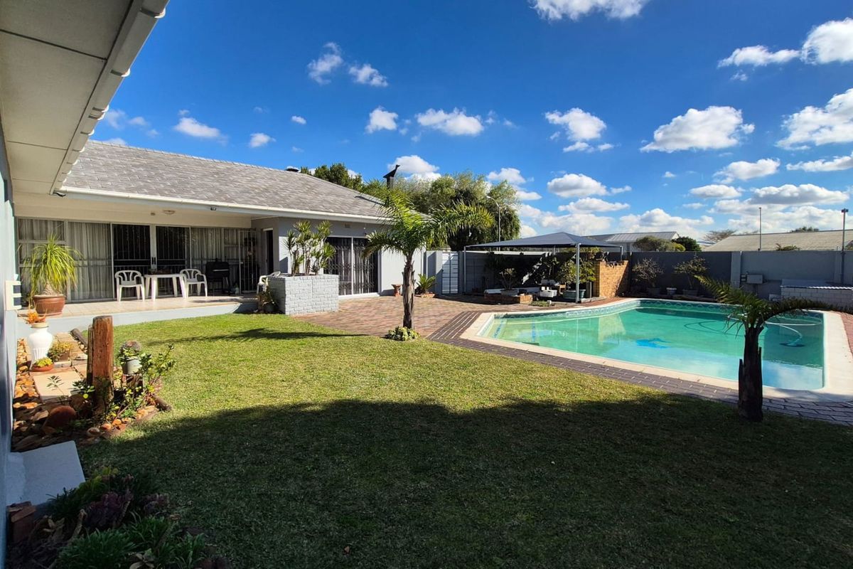 Spacious rear garden featuring a swimming pool, paved patio area, and well-maintained lawn, perfect for outdoor entertaining.