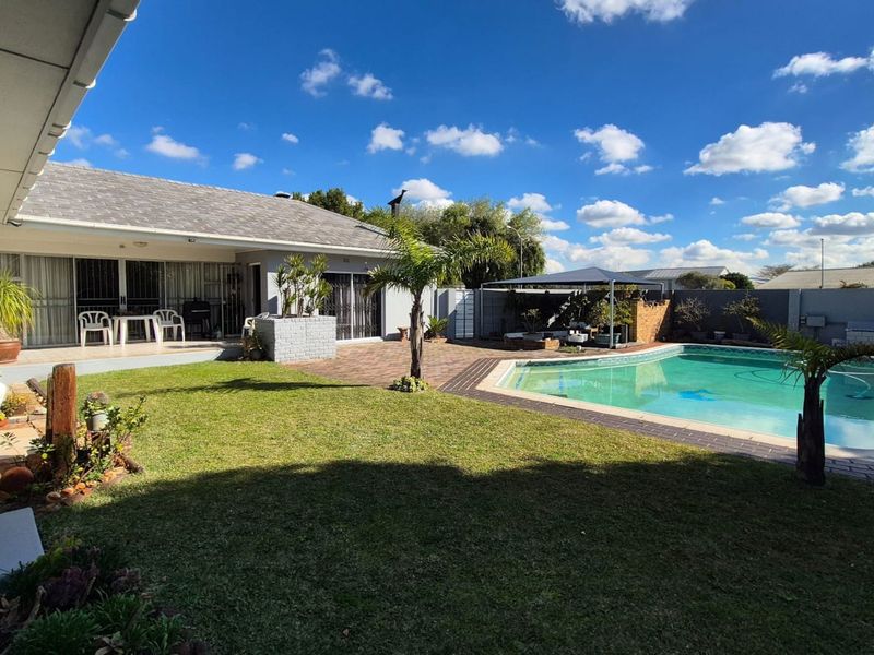 Spacious rear garden featuring a swimming pool, paved patio area, and well-maintained lawn, perfect for outdoor entertaining.