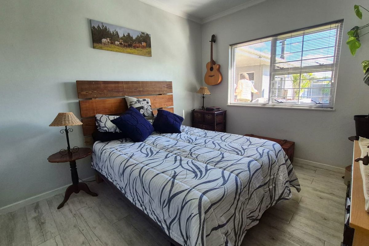 A well-lit bedroom featuring light-toned laminate flooring, neutral wall finishes, and a large window with fitted venetian blinds.