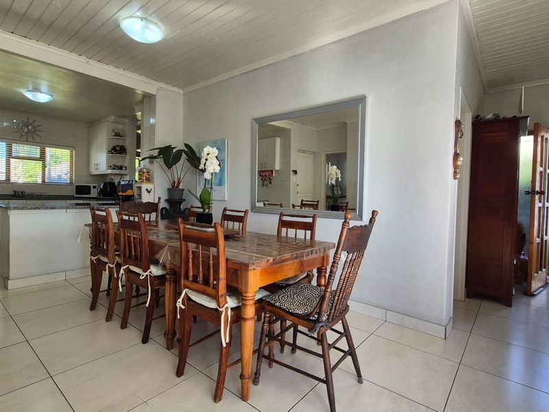 Open-plan dining area flowing into a functional kitchen with granite countertops, tiled flooring, and a classic tongue and groove ceiling.