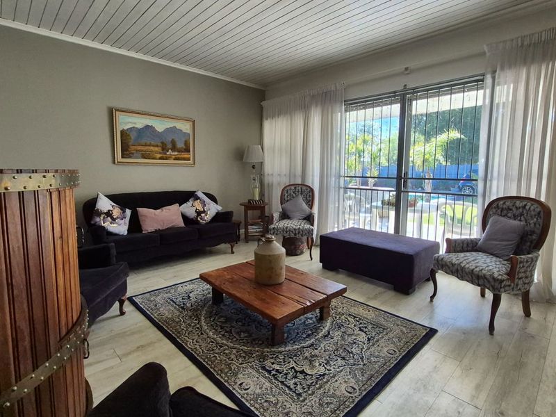 A comfortable living room featuring laminate flooring, a tongue and groove ceiling, and large sliding glass doors with security gates leading to the garden.