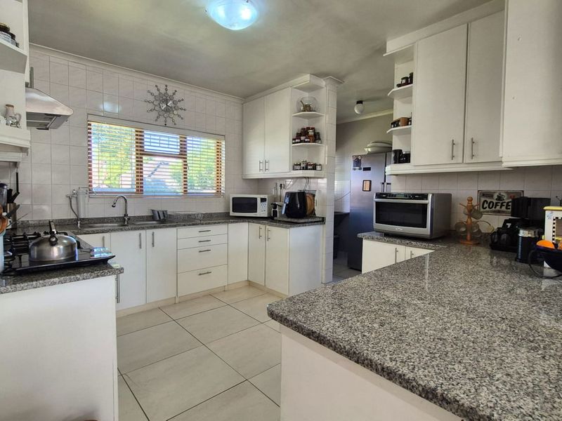 A functional kitchen featuring granite countertops, white cabinetry, a gas hob with extractor fan, and tiled flooring throughout.