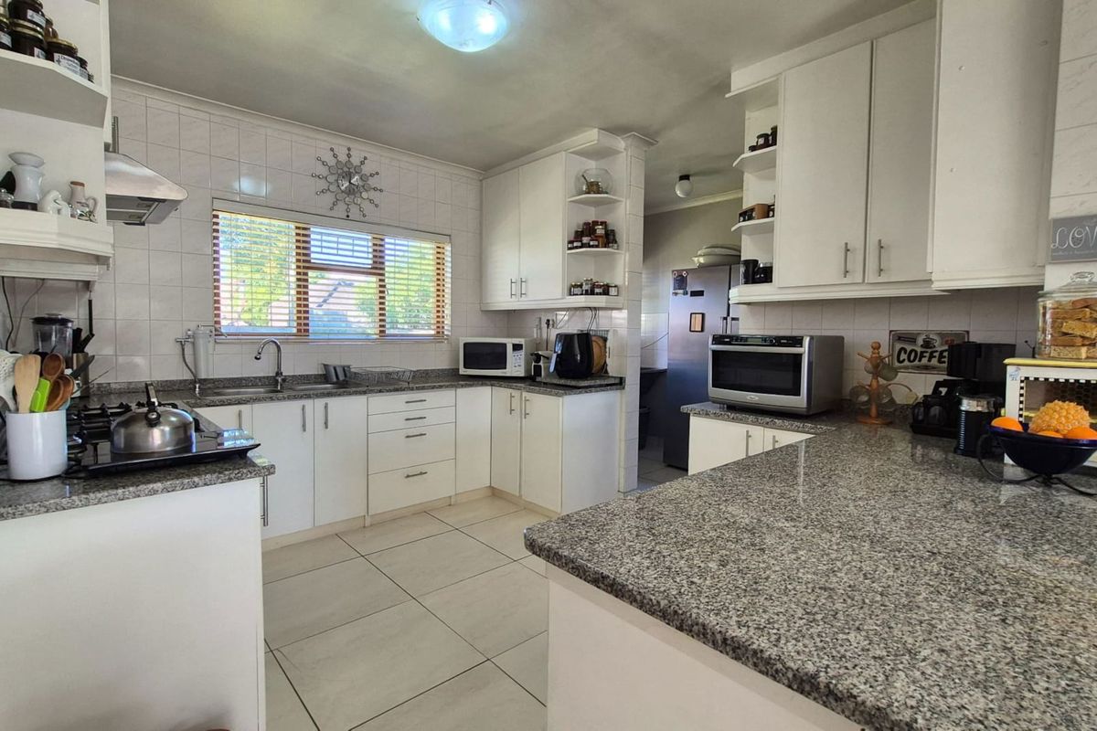 A functional kitchen featuring granite countertops, white cabinetry, a gas hob with extractor fan, and tiled flooring throughout.