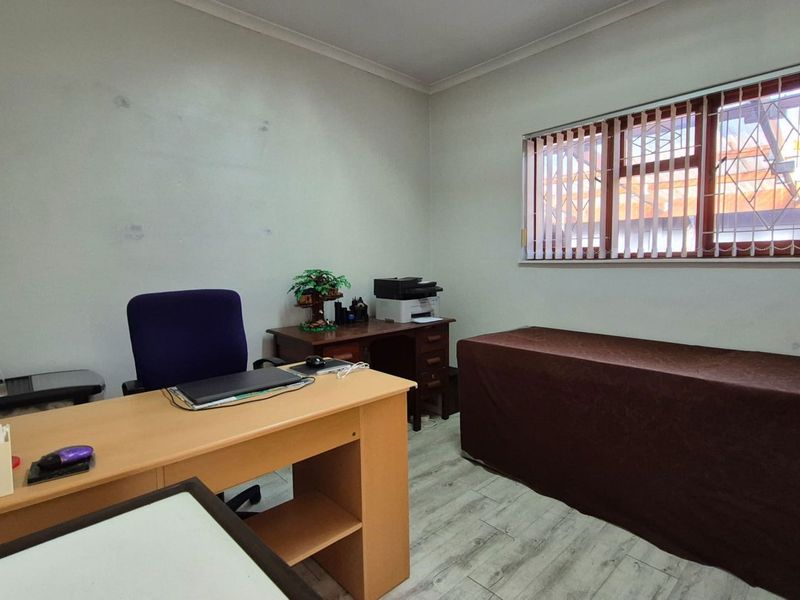 A functional home office space featuring laminate flooring, a window with security bars, and vertical blinds.