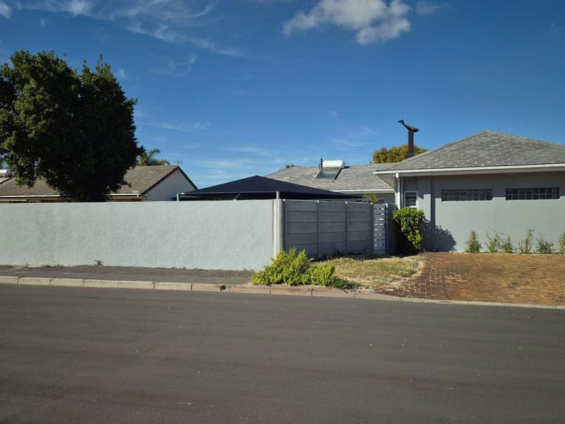 Front exterior view of the property featuring a paved driveway, precast concrete boundary wall, and solar water heating system on the roof.