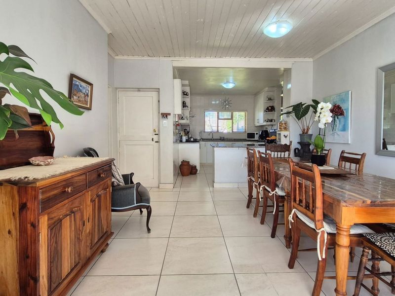 Open-plan living and dining area flowing into a functional kitchen with tiled floors and timber ceiling details.