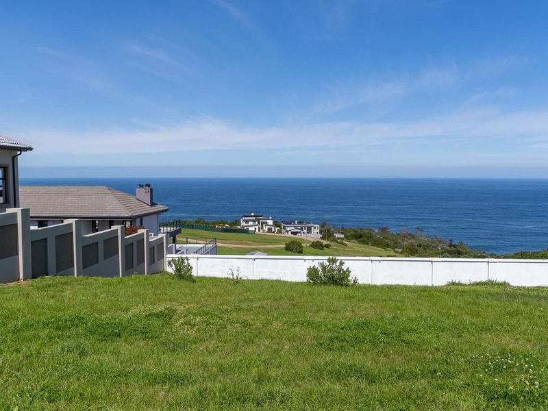 A scenic view of the ocean from a residential plot, featuring a well-maintained lawn and boundary wall.
