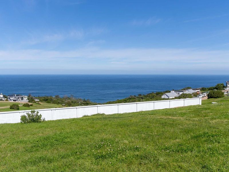 A scenic view of the ocean from a vacant residential plot, featuring a clear boundary wall and expansive coastal landscape.