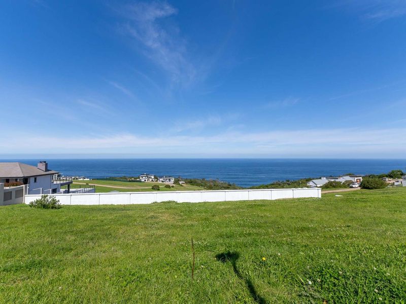 A scenic view of the ocean and coastal landscape from a vacant residential plot, featuring a clear horizon and surrounding neighborhood.