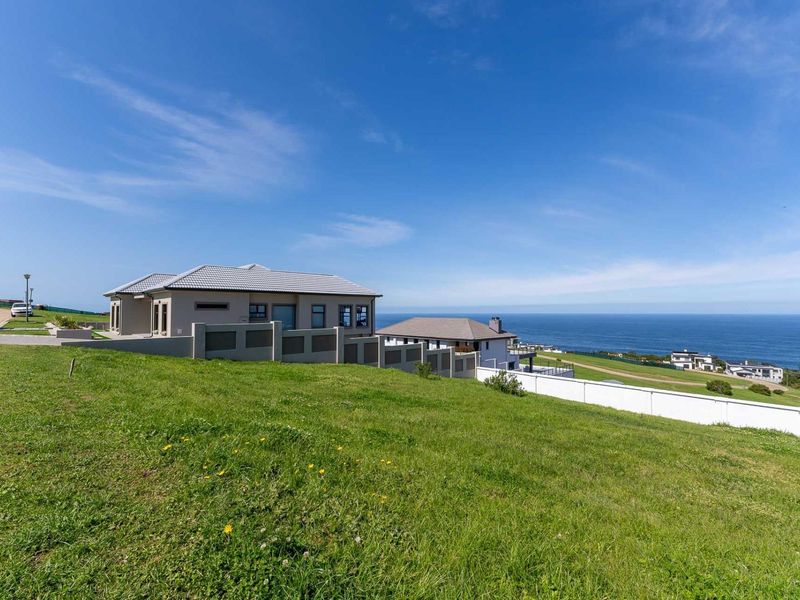 A view of a modern residential property featuring a well-maintained lawn, boundary wall, and scenic coastal views in a quiet neighborhood.