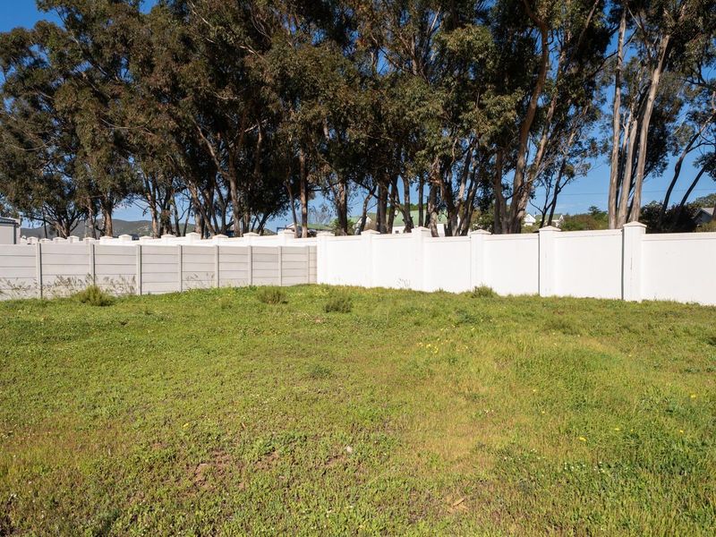 A vacant residential plot featuring a level grassed area enclosed by a secure precast concrete boundary wall and mature perimeter trees.