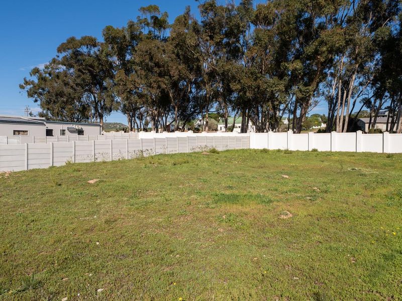 A vacant residential plot featuring a level grassed area enclosed by a secure precast concrete boundary wall with mature trees in the background.