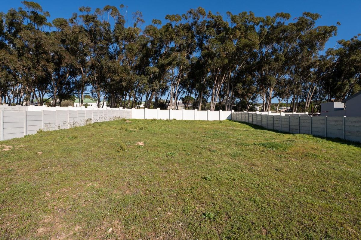 A level, vacant residential plot enclosed by precast concrete boundary walls, featuring established trees along the rear perimeter.
