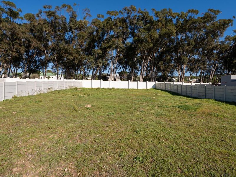 A level, vacant residential plot enclosed by precast concrete boundary walls, featuring established trees along the rear perimeter.