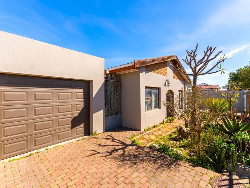 Front view of the property featuring a paved driveway, single garage, and established garden area.