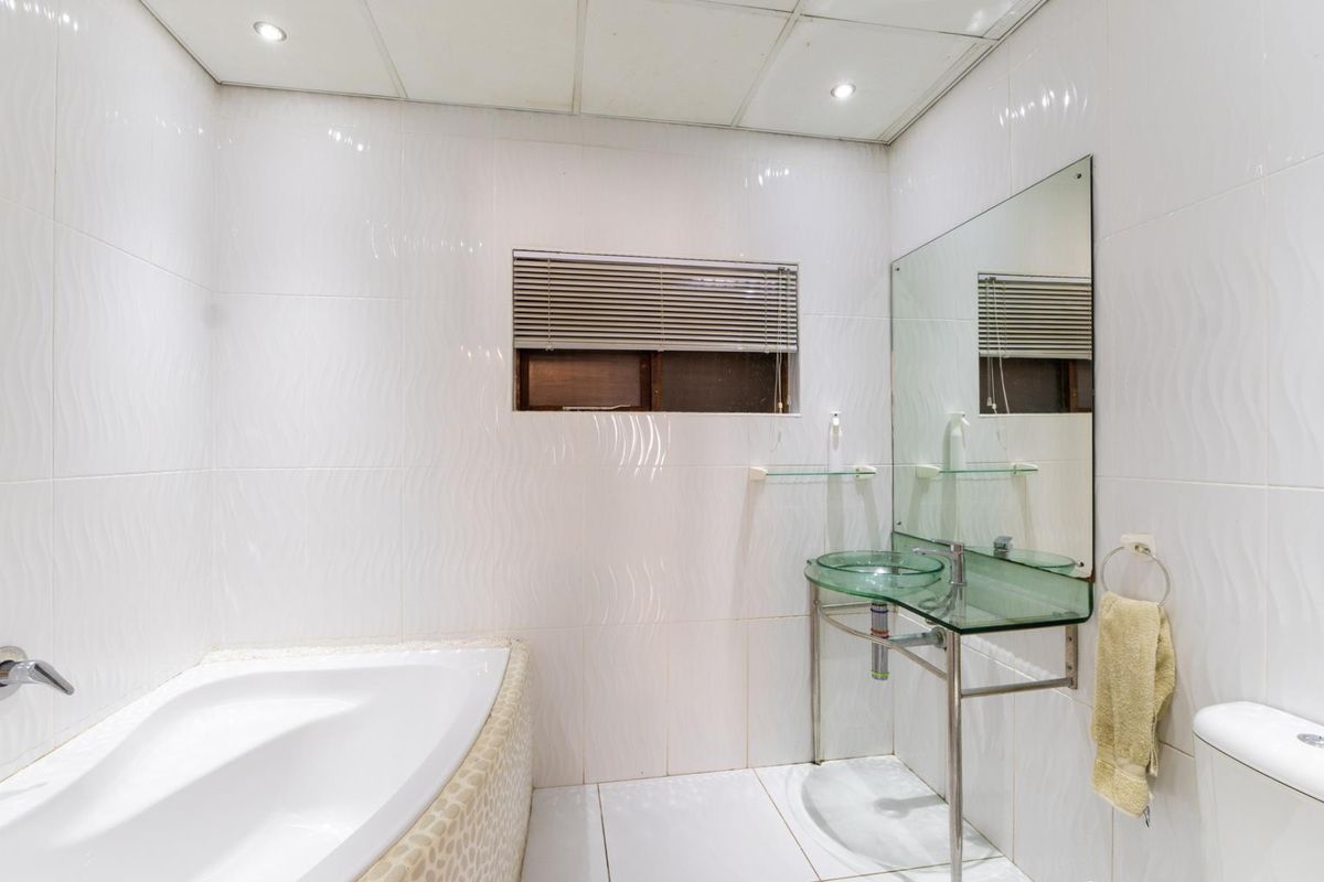 A clean, white-tiled bathroom featuring a built-in bathtub, a modern glass vessel sink with a metal vanity frame, and a wall-mounted mirror.
