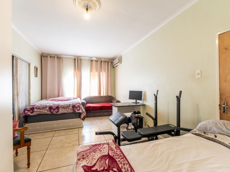 A spacious bedroom featuring tiled flooring, an air conditioning unit, and a ceiling rose, currently utilized as a multi-purpose living and exercise space.