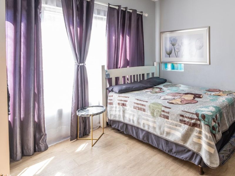 A well-lit bedroom featuring laminate flooring and a large window with curtains, providing a comfortable and functional living space.