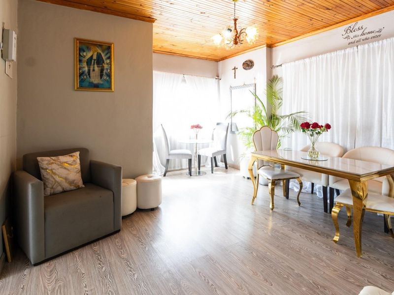 A dining area featuring timber ceiling paneling, laminate flooring, and a central chandelier, providing a functional space for meals and gatherings.