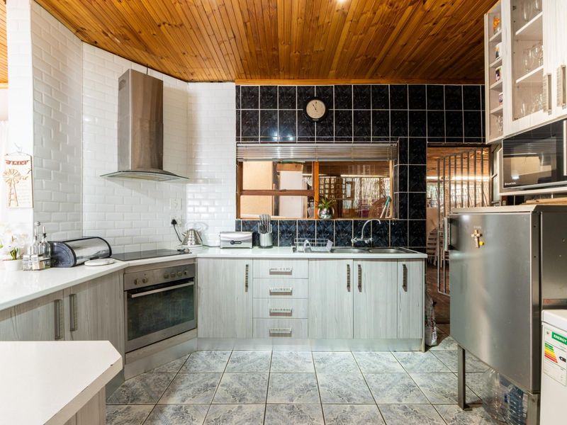 A functional kitchen featuring light wood-finish cabinetry, a stainless steel extractor fan, built-in oven, tiled backsplash, and a distinctive timber-paneled ceiling.