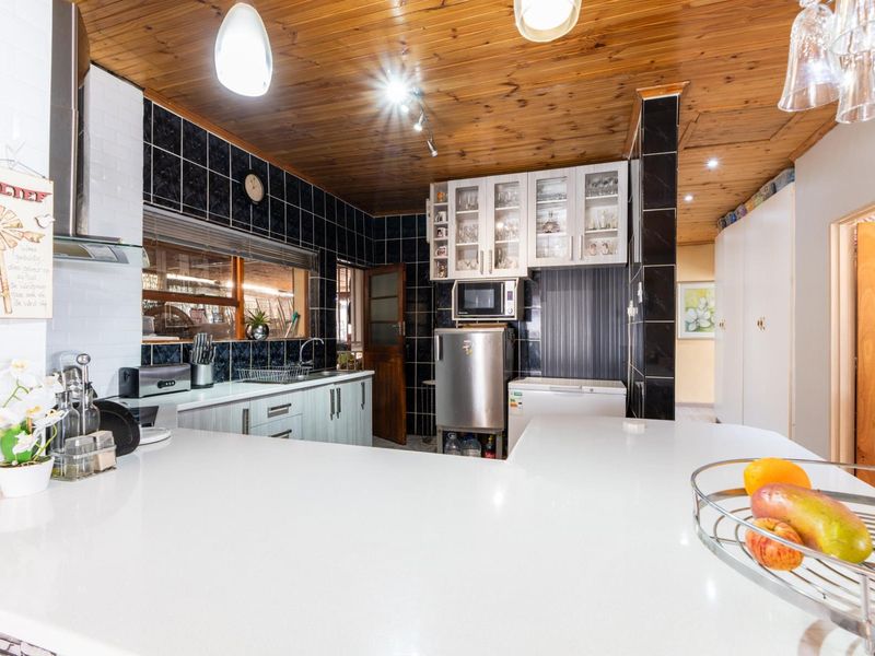 A functional kitchen featuring a breakfast bar, timber ceiling, built-in cabinetry, and a tiled backsplash, offering a practical layout for daily meal preparation.