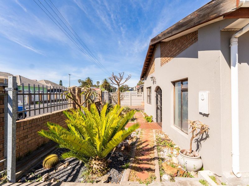 Front exterior view of the property featuring a brick boundary wall, steel security fencing, and a paved pathway leading to the entrance.