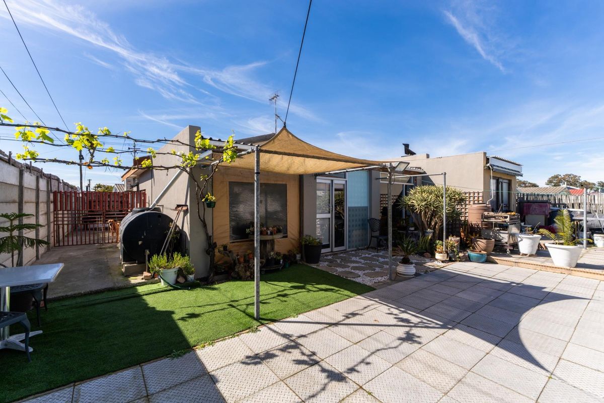Rear exterior view featuring a paved patio area, artificial lawn, and a shade sail structure attached to the building.