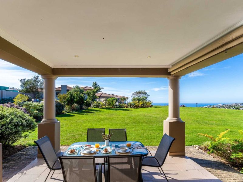 A spacious covered patio featuring tiled flooring and structural columns, offering expansive views over the lush garden and distant ocean horizon.