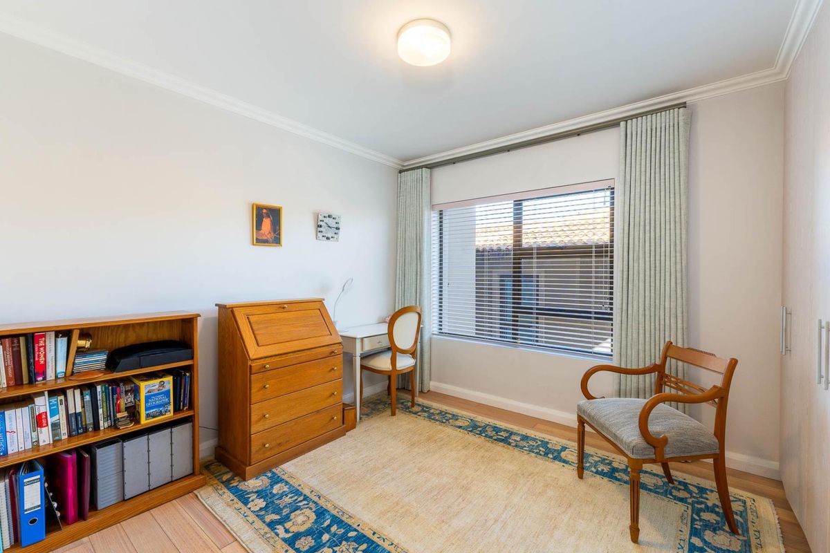 A well-maintained bedroom featuring timber flooring, built-in wardrobe storage, and large windows with venetian blinds and curtains.