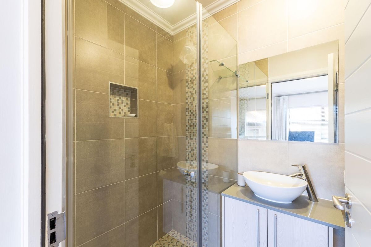 Modern bathroom featuring a glass-enclosed shower with mosaic tile accents, a sleek vessel sink, and a vanity cabinet with a wall-mounted mirror.