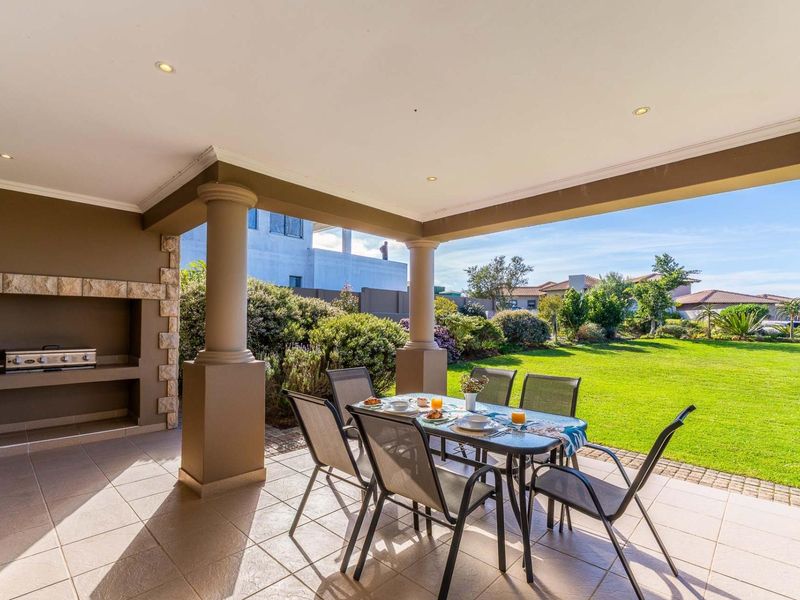 Covered patio featuring a built-in braai, stone cladding, and tiled flooring, overlooking a well-maintained garden.