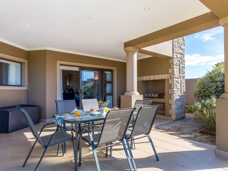 A covered patio featuring tiled flooring, recessed lighting, and a built-in stone-clad braai area, providing seamless access to the interior through sliding glass doors.