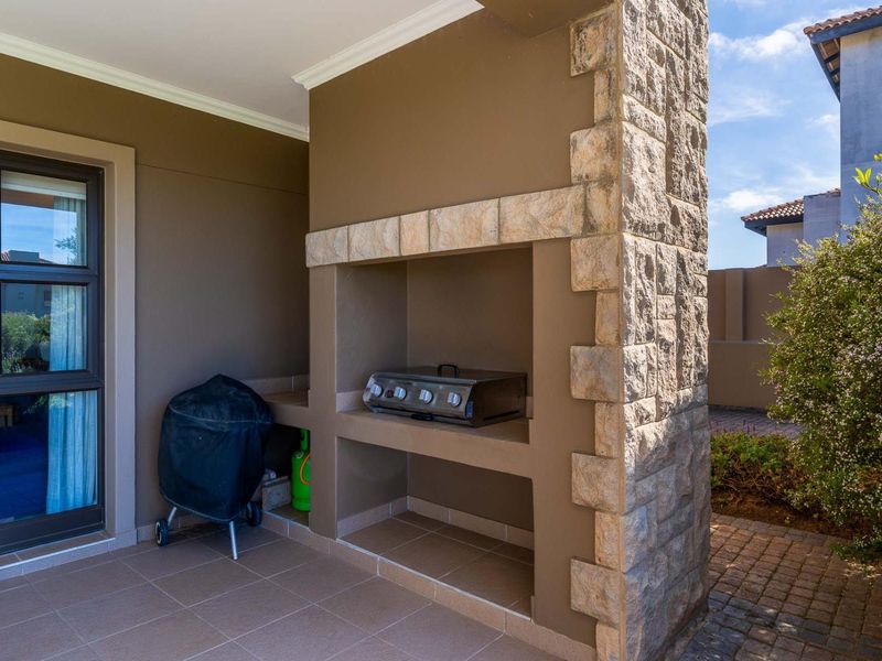 Covered patio area featuring a built-in braai with stone cladding detail and tiled flooring, providing a functional outdoor entertainment space.