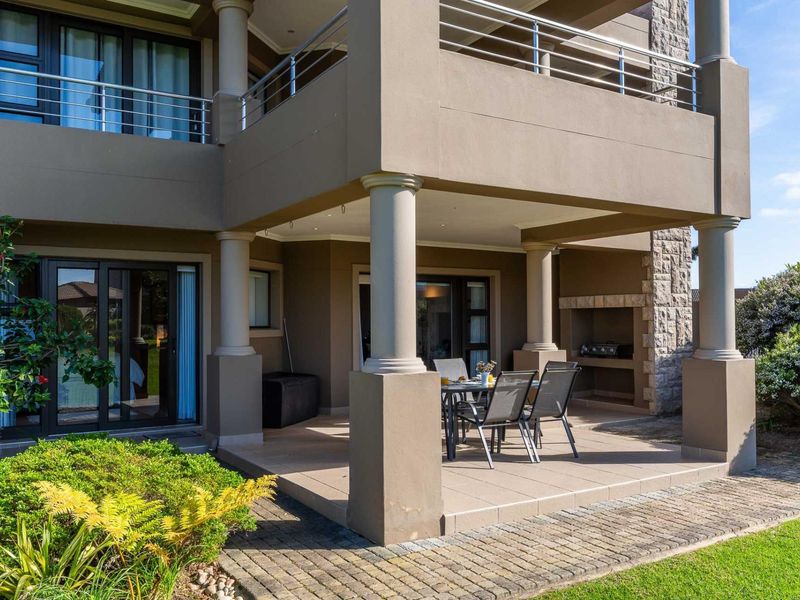 Covered ground floor patio featuring a built-in braai, stone cladding accents, and tiled flooring, providing a seamless transition to the garden area.