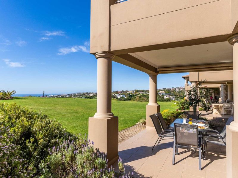 A spacious covered patio featuring tiled flooring and structural columns, offering expansive views over a manicured lawn and the surrounding landscape.