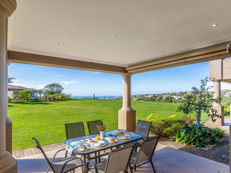 A spacious covered patio featuring tiled flooring and structural columns, offering expansive views over the manicured garden and distant ocean horizon.