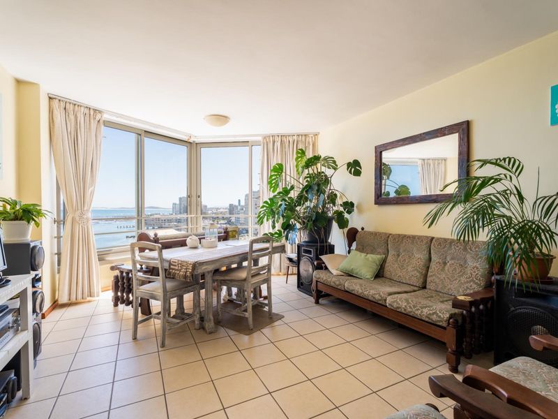 Open-plan living and dining area featuring large floor-to-ceiling windows with expansive coastal views and ceramic tile flooring throughout.