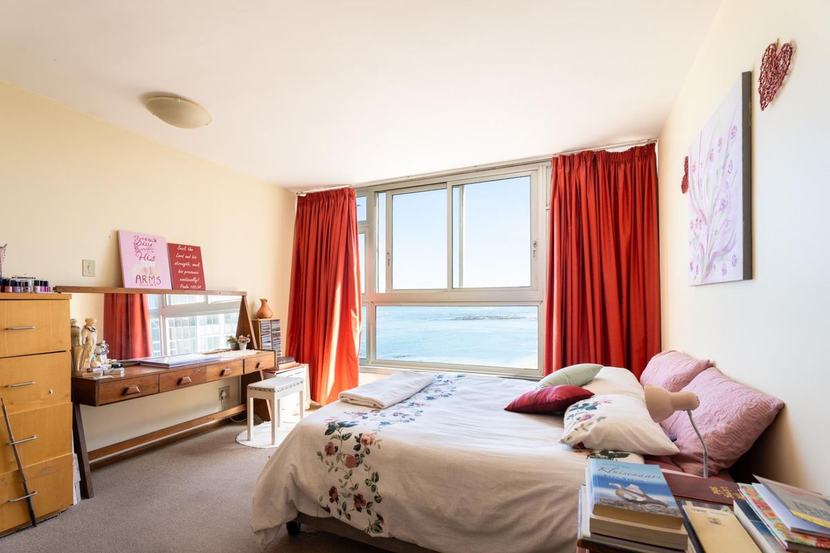 A bright bedroom featuring large sliding windows with expansive ocean views and neutral carpet flooring.