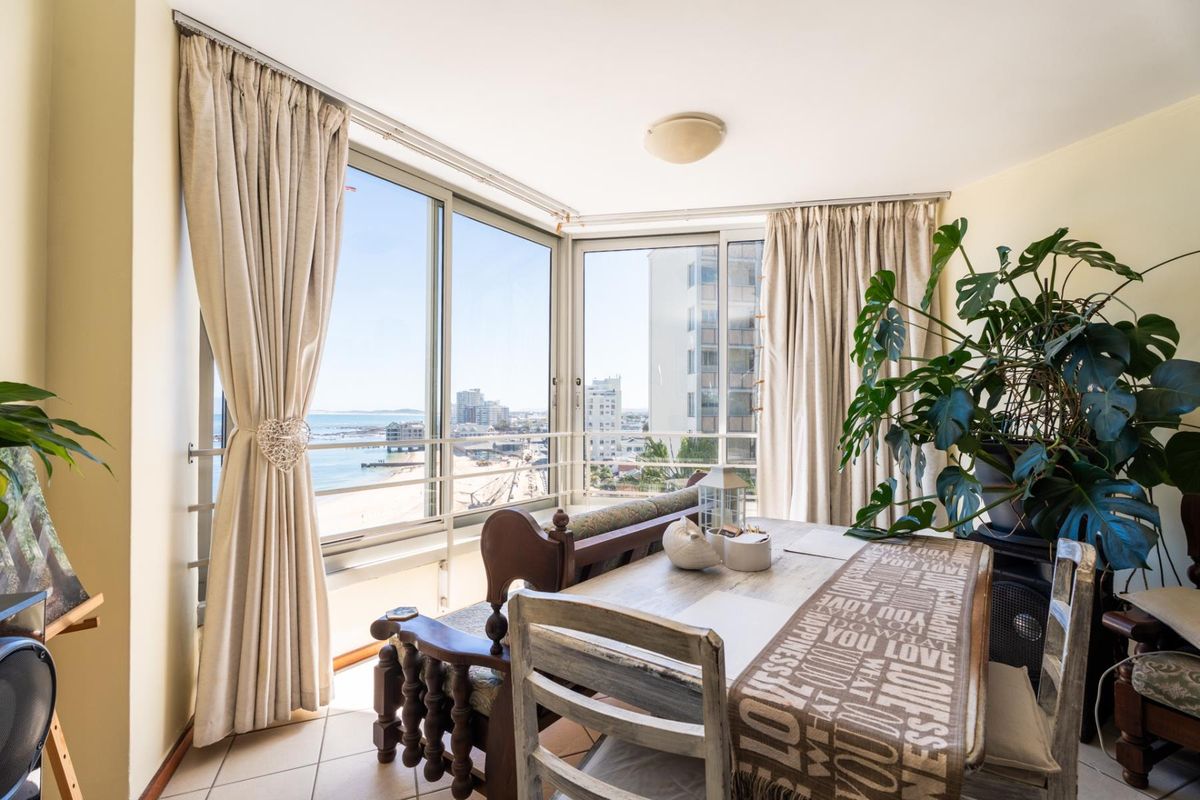 A bright living area featuring large sliding glass doors that offer expansive coastal and urban views, complemented by neutral tiled flooring.