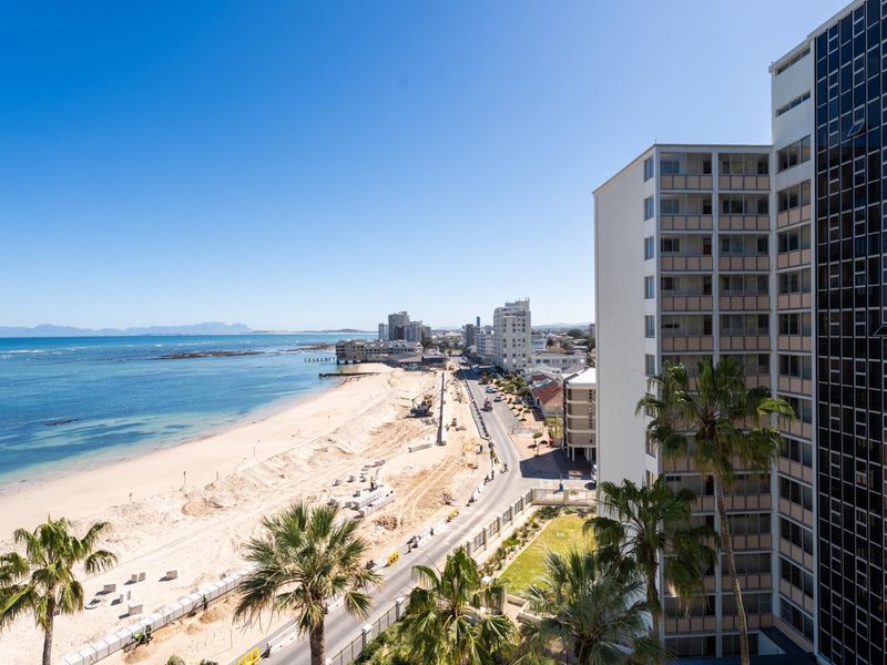 Elevated coastal view overlooking the beach, promenade, and surrounding apartment buildings.
